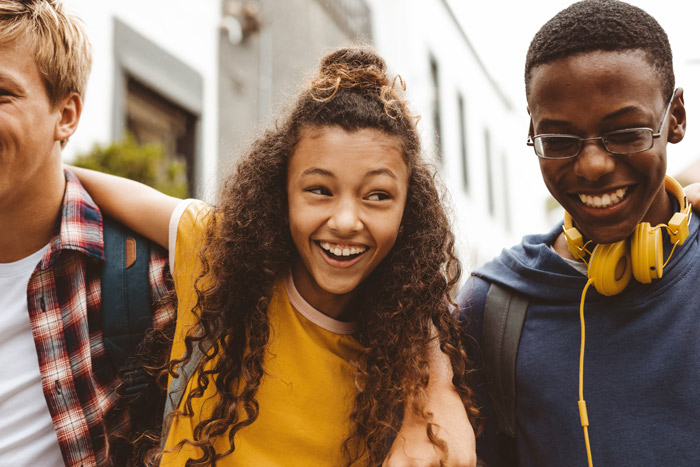 Three smiling teenagers standing close together, enjoying time outdoors, with a focus on their friendship and laughter.